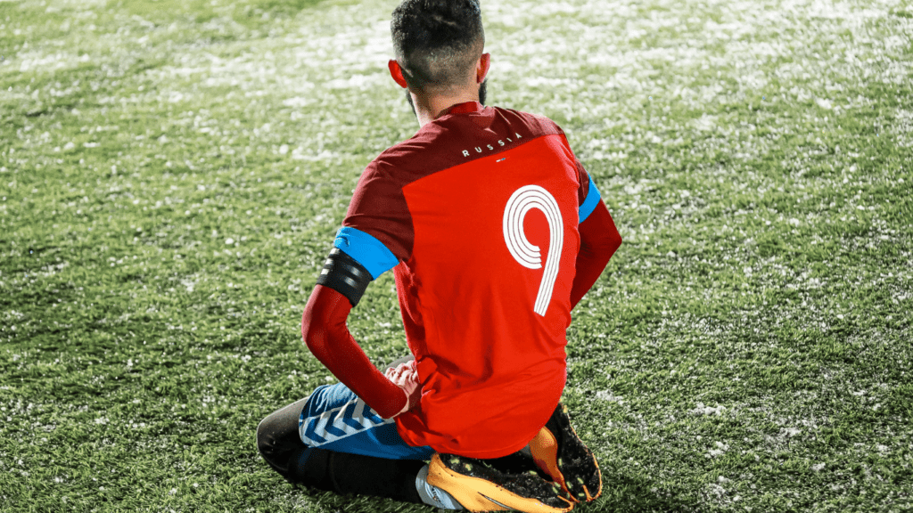 a soccer player sitting on the ground with their hands on their knees