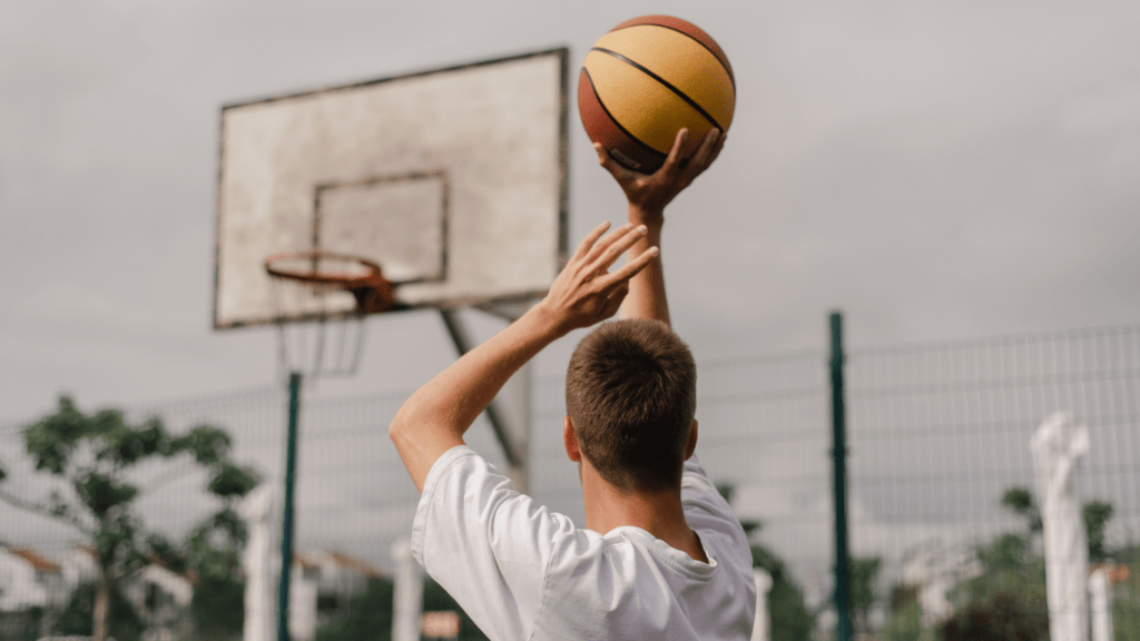 A person is holding up a basketball in front of a fence